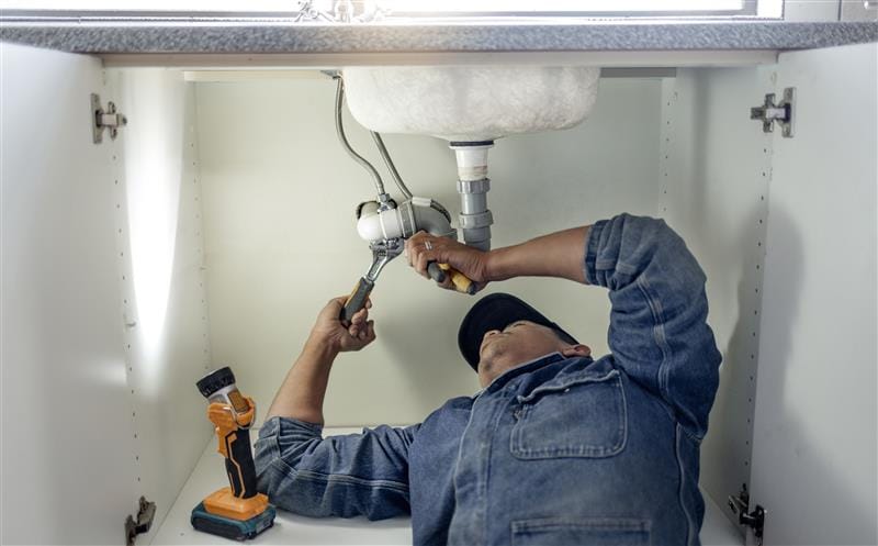 Plumber repairing pipes beneath a bathroom sink in Camarillo